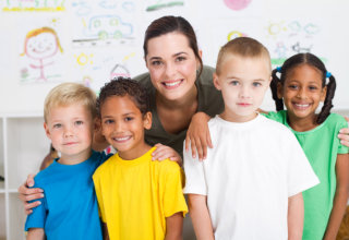 A happy preschool class posing with their teacher in classroom